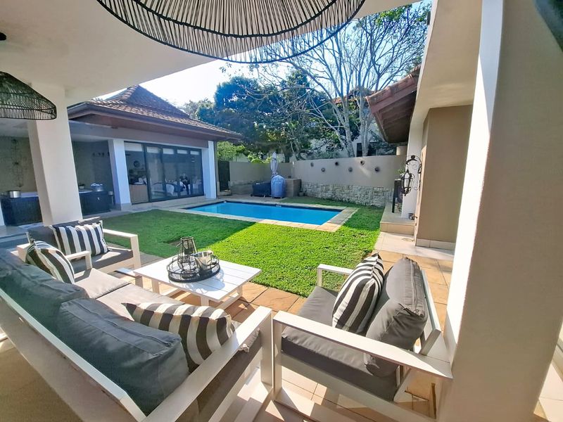A covered patio area overlooking a private swimming pool and landscaped garden, featuring tiled flooring and direct access to the main residence.