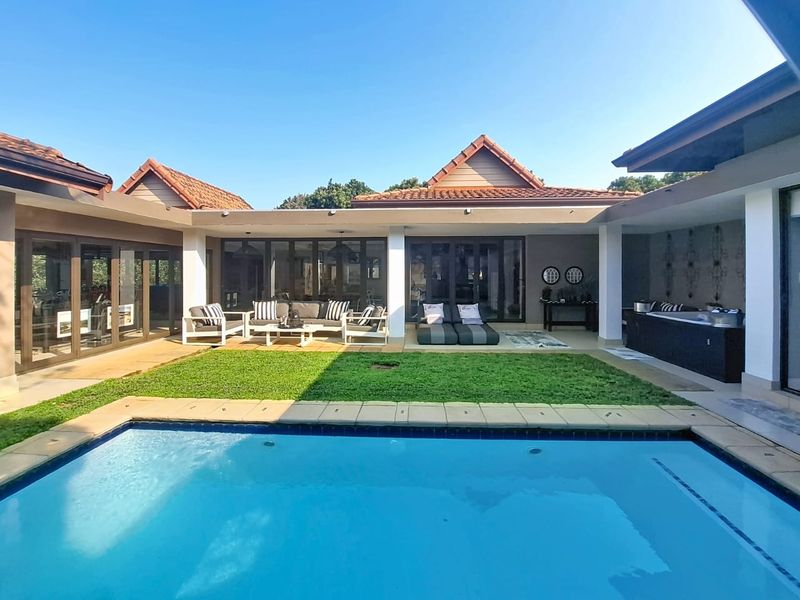 A well-maintained outdoor entertainment area featuring a swimming pool, a central lawn, and a spacious covered patio with direct access to the home.