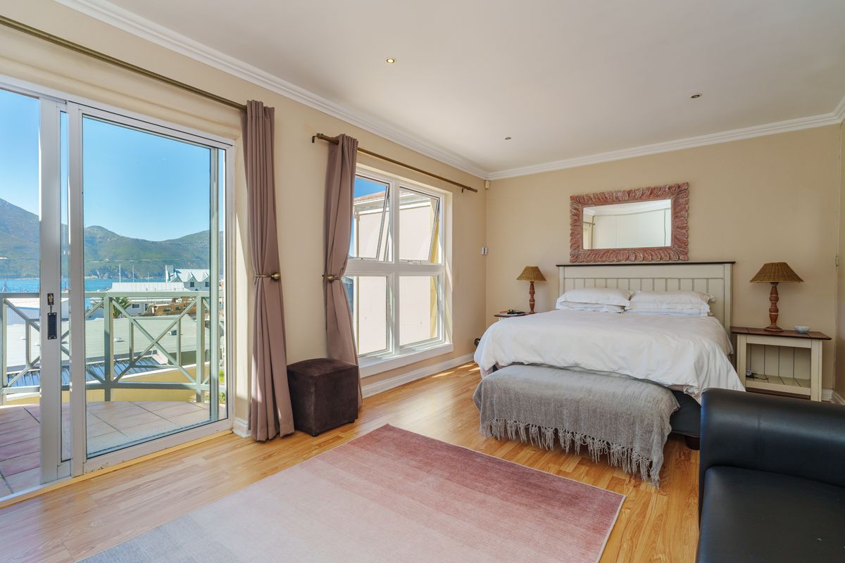 Spacious bedroom featuring light wood flooring, crown molding, and large sliding glass doors opening to a private balcony with scenic coastal views.