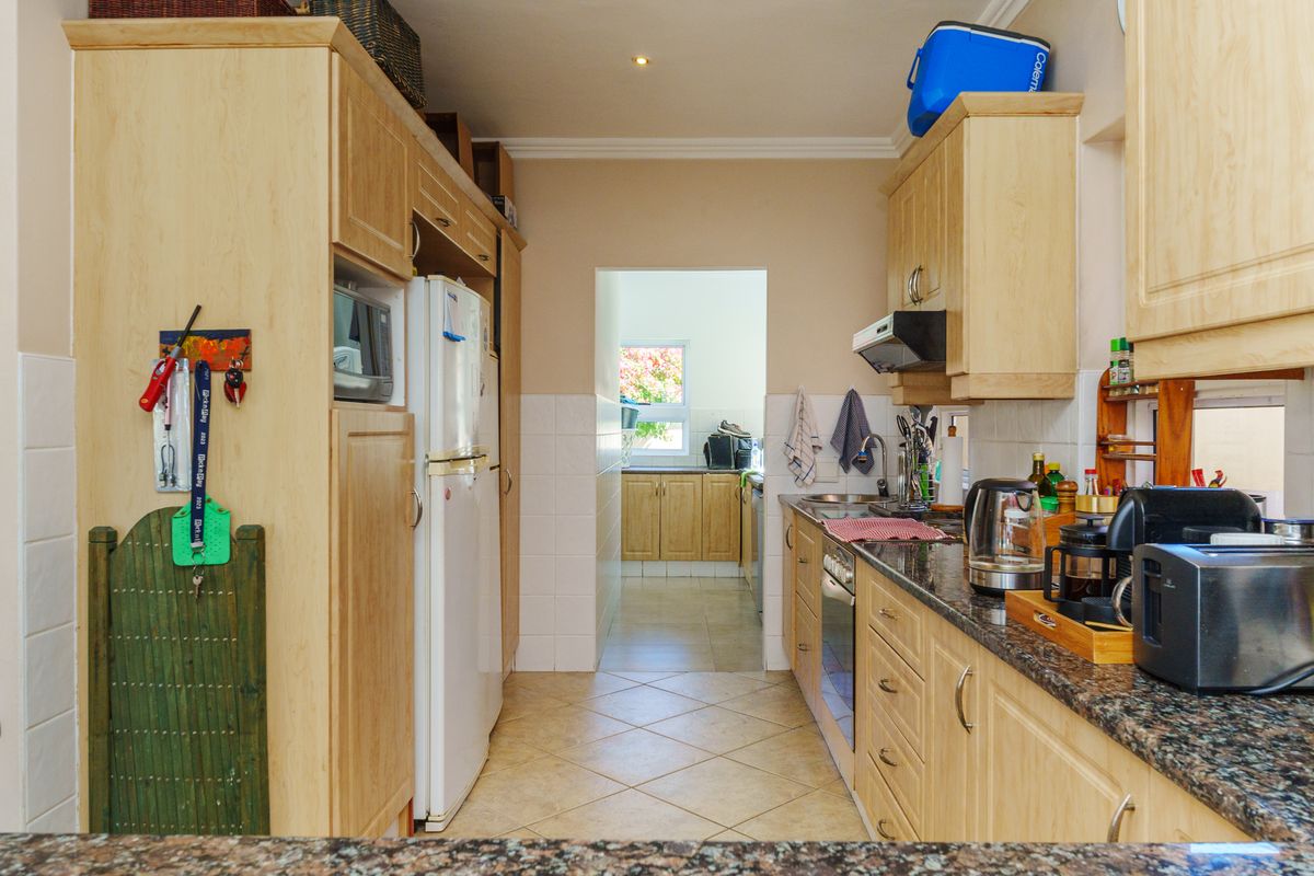 A functional kitchen featuring light wood cabinetry, granite countertops, and tiled flooring, with a direct view into an adjacent scullery area.