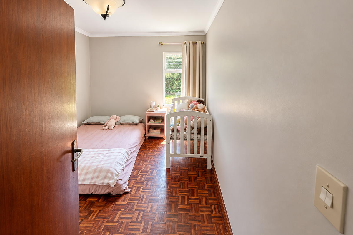 A cozy bedroom featuring warm parquet flooring, a single window for natural light, and a neutral wall finish.