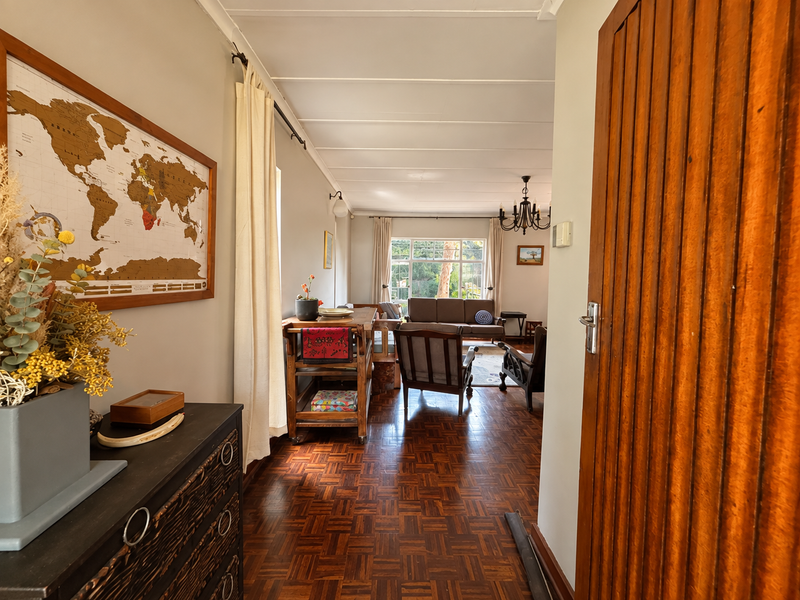 A view from the entrance into a bright living area featuring classic parquet flooring, large windows, and a warm, inviting atmosphere.