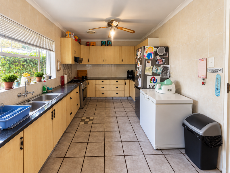 Functional kitchen featuring light wood cabinetry, tiled walls, double basin sink, and ceramic tile flooring with a ceiling fan.