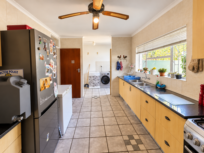 A functional kitchen featuring light wood cabinetry, granite countertops, tiled flooring, and a ceiling fan, with an adjacent laundry area visible.