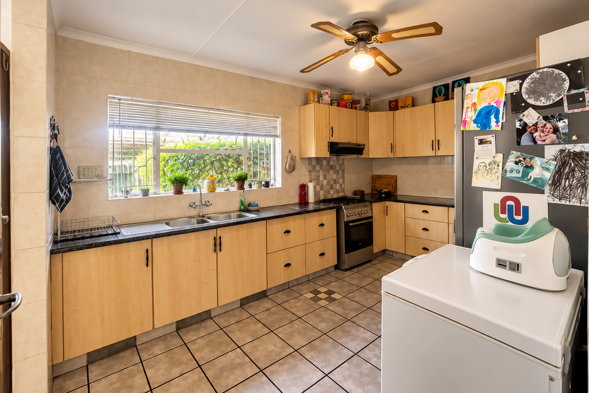 Functional kitchen featuring light wood-look cabinetry, tiled splashbacks, double sink, and a freestanding oven, offering a practical layout with ample storage space.