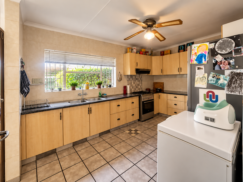 Functional kitchen featuring light wood-look cabinetry, tiled splashbacks, double sink, and a freestanding oven, offering a practical layout with ample storage space.