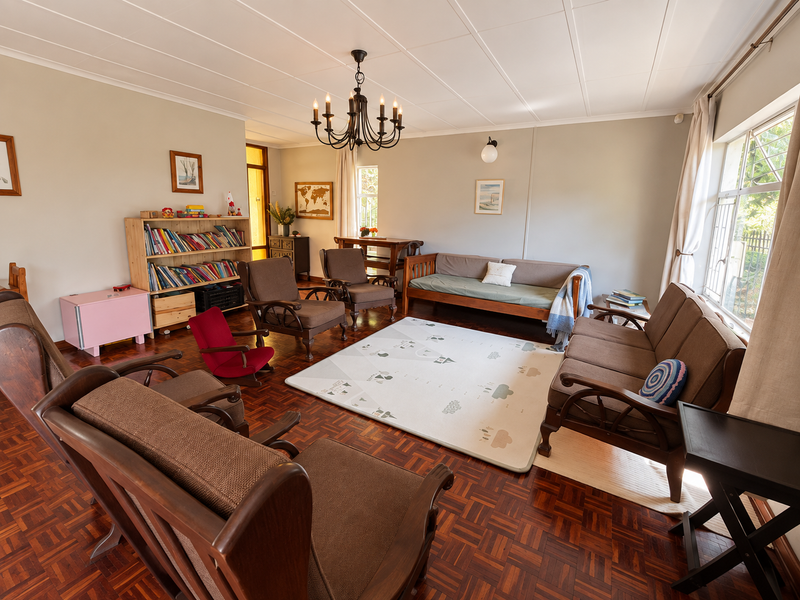 A spacious living room featuring classic parquet flooring, a decorative wrought iron chandelier, and large steel-framed windows providing natural light.