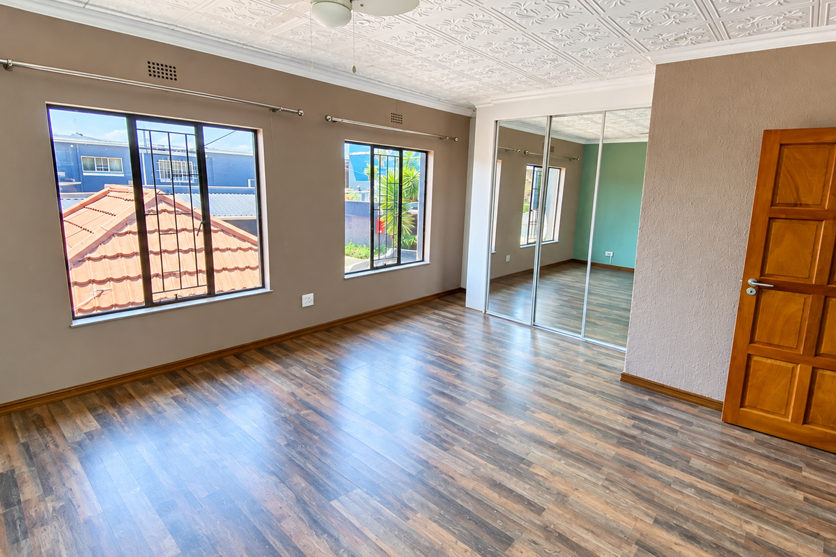 Spacious bedroom featuring laminate flooring, built-in mirrored wardrobes, and a decorative pressed metal ceiling, offering a bright and functional living space.