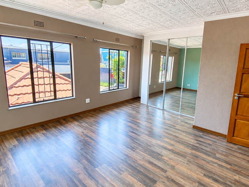 Spacious bedroom featuring laminate flooring, built-in mirrored wardrobes, and a decorative pressed metal ceiling, offering a bright and functional living space.
