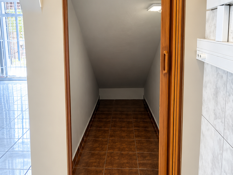 A compact under-stair utility storage space featuring tiled flooring and a folding door, accessible from the main living area.