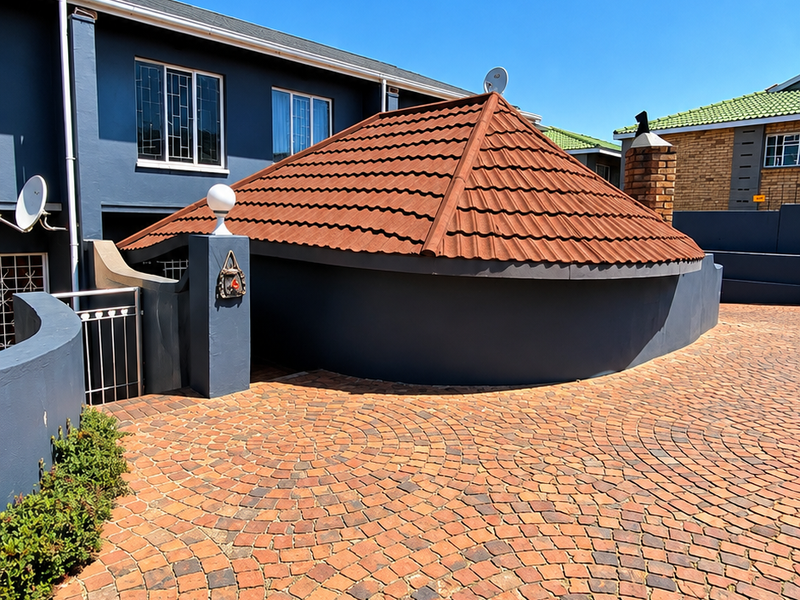 Front exterior view of the townhouse featuring a unique circular roof design, brick paved driveway, and secure gated entrance.
