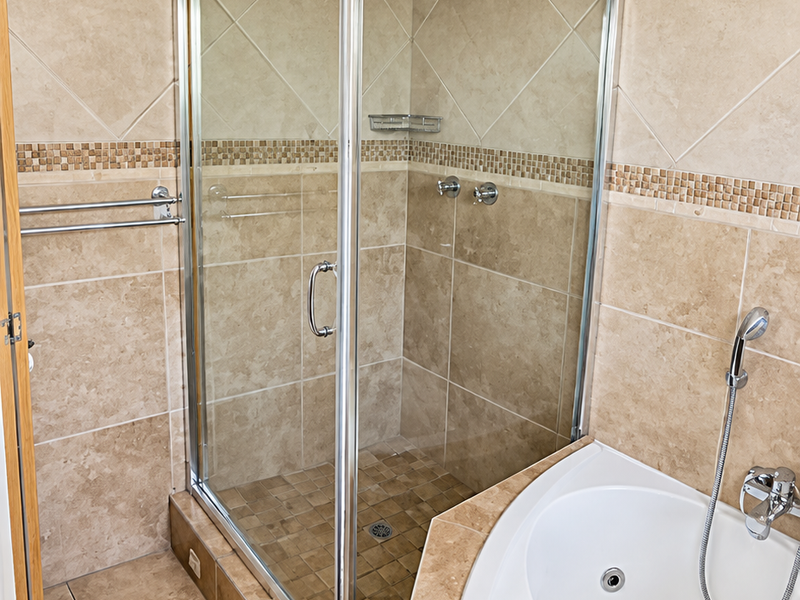 A well-maintained bathroom featuring a corner shower enclosure with glass doors and a built-in corner bathtub with tiled surround and mosaic accents.