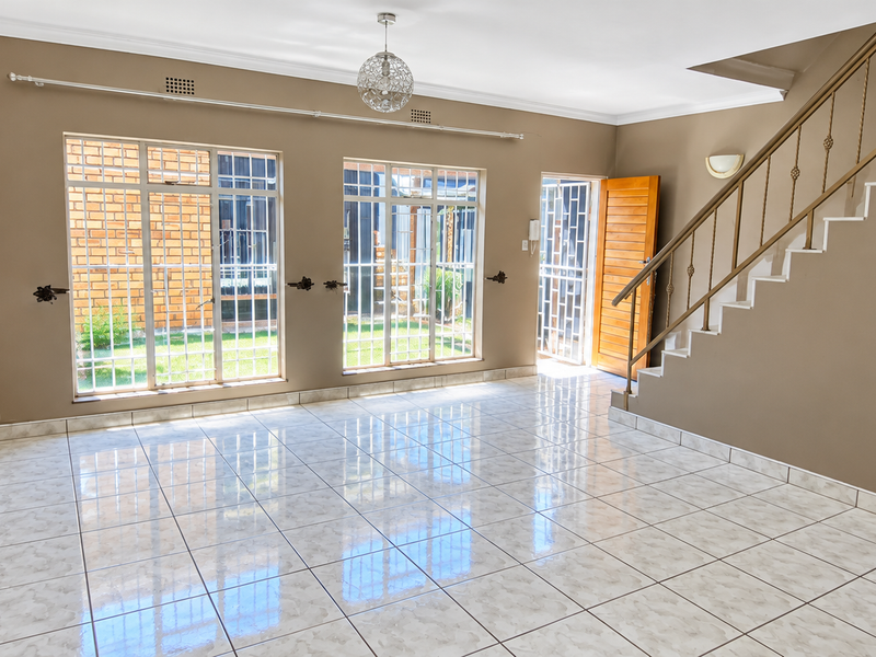 Spacious, empty living area featuring tiled flooring, a staircase with metal railing, and large windows with security bars, offering a bright and open layout.
