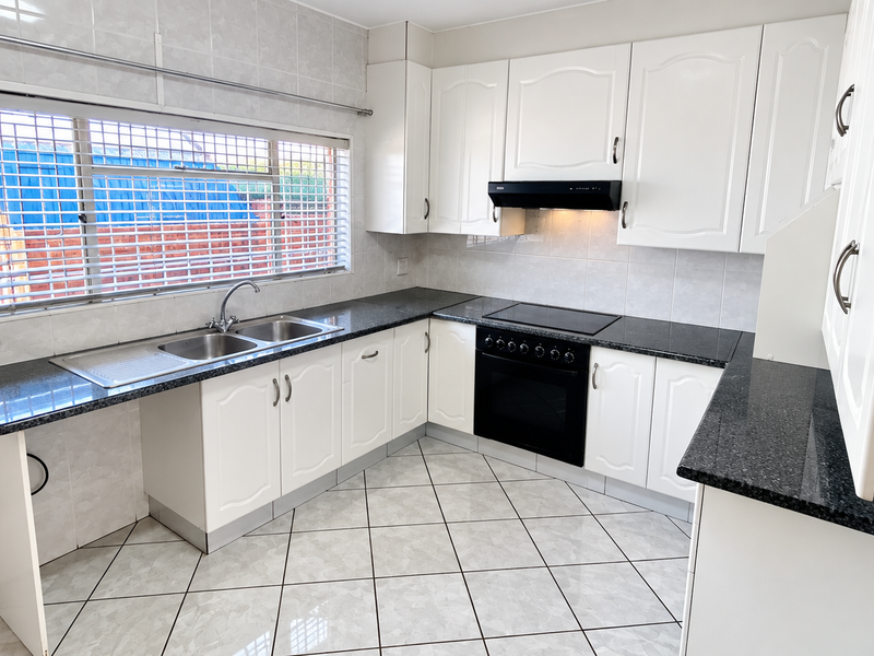 A clean, functional kitchen featuring white cabinetry, granite countertops, built-in oven with hob, and tiled finishes throughout.