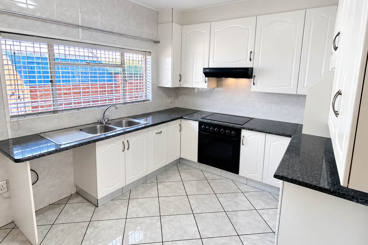 A clean, functional kitchen featuring white cabinetry, granite countertops, built-in oven with hob, and tiled finishes throughout.
