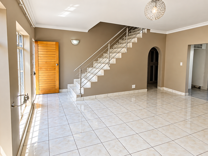 Spacious, light-filled living area featuring polished tiled floors, a modern staircase with stainless steel railings, and large windows providing ample natural light.