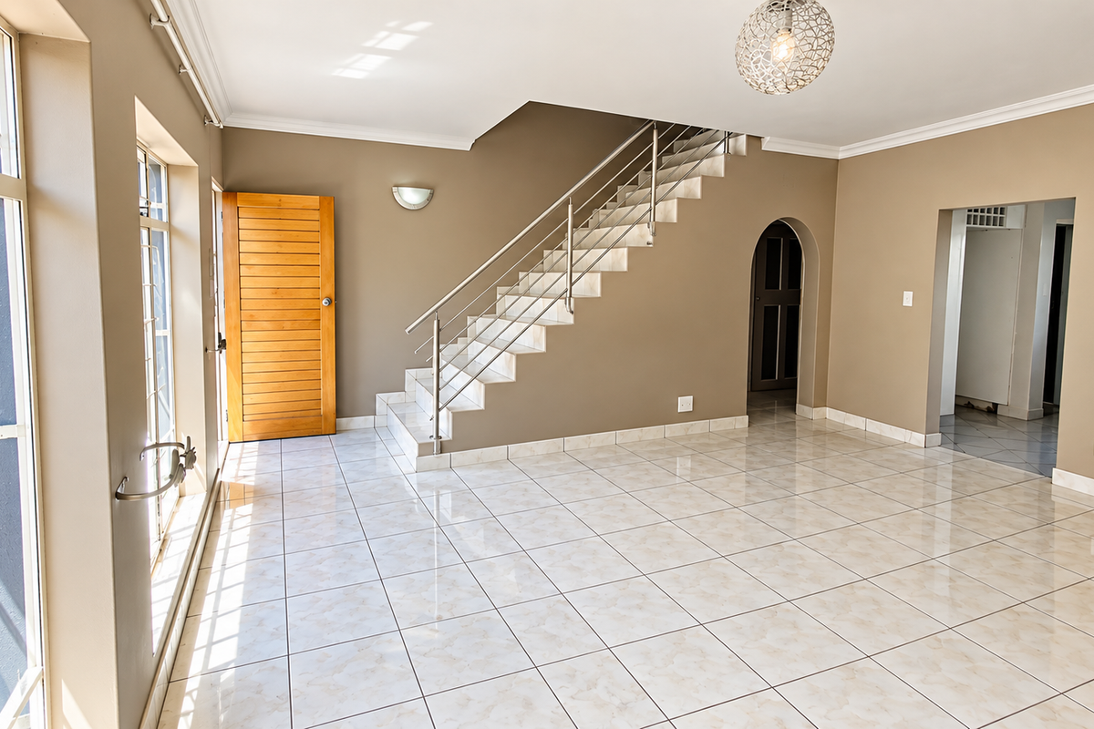Spacious, light-filled living area featuring polished tiled floors, a modern staircase with stainless steel railings, and large windows providing ample natural light.