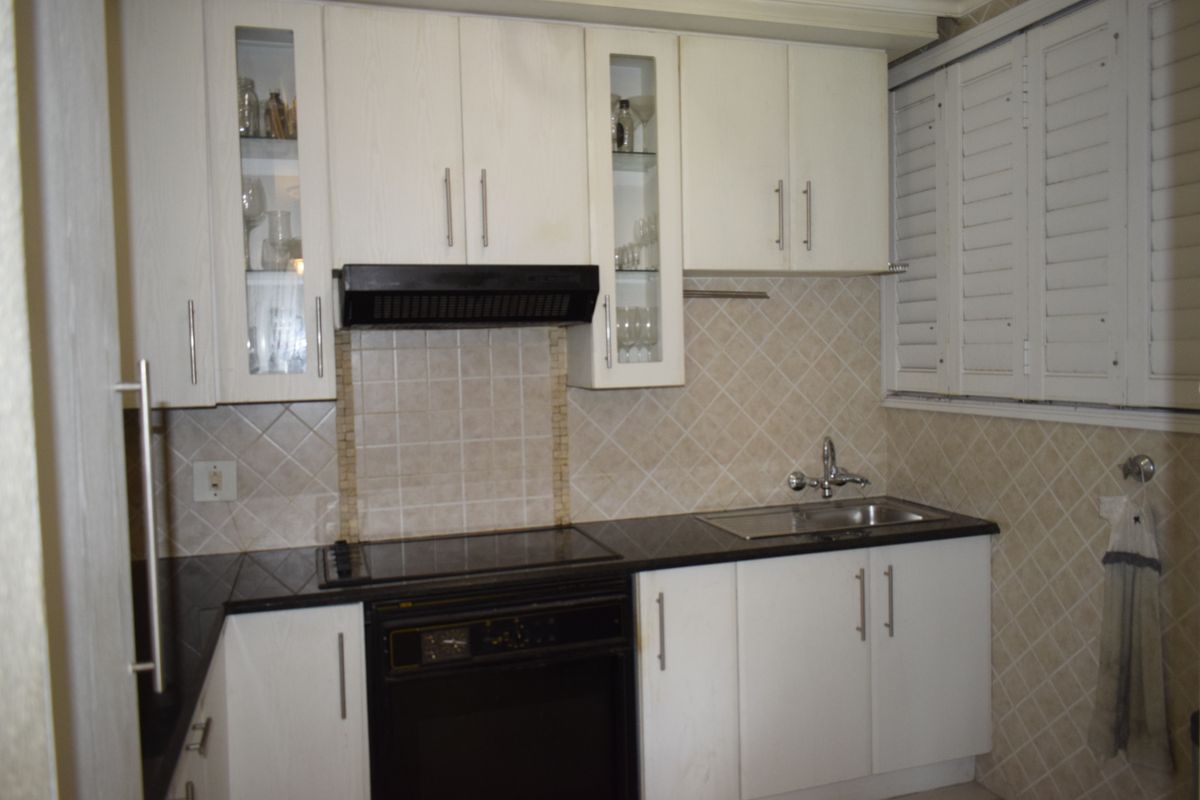 A functional kitchen featuring white cabinetry, black granite countertops, integrated oven, electric hob, and classic tiled backsplash with plantation shutters.
