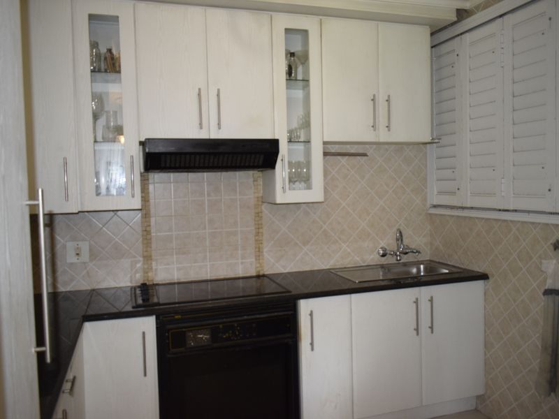 A functional kitchen featuring white cabinetry, black granite countertops, integrated oven, electric hob, and classic tiled backsplash with plantation shutters.