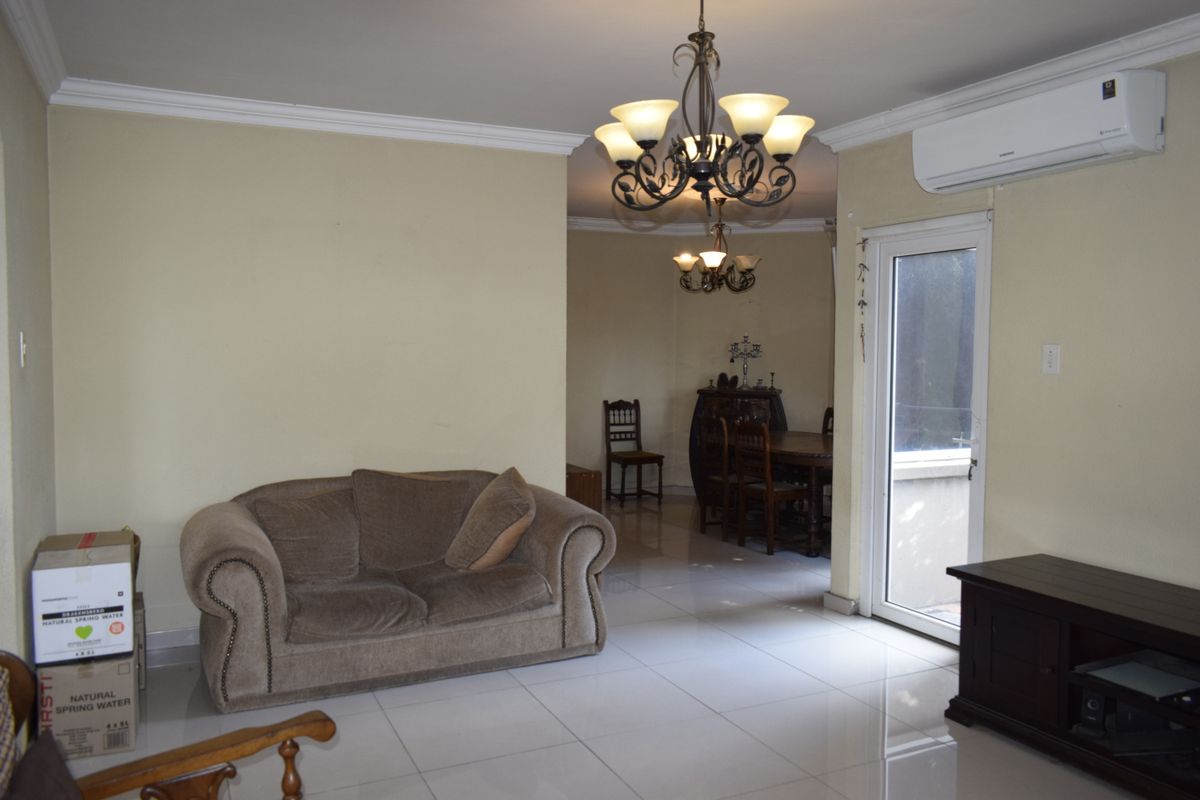 A living room featuring tiled flooring, crown molding, a wall-mounted air conditioning unit, and a decorative chandelier, with access to an outdoor area.