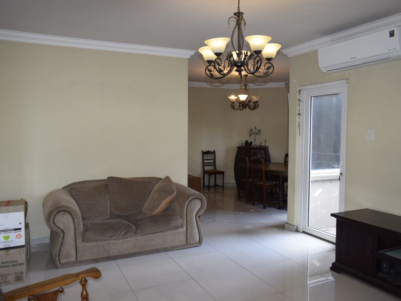 A living room featuring tiled flooring, crown molding, a wall-mounted air conditioning unit, and a decorative chandelier, with access to an outdoor area.