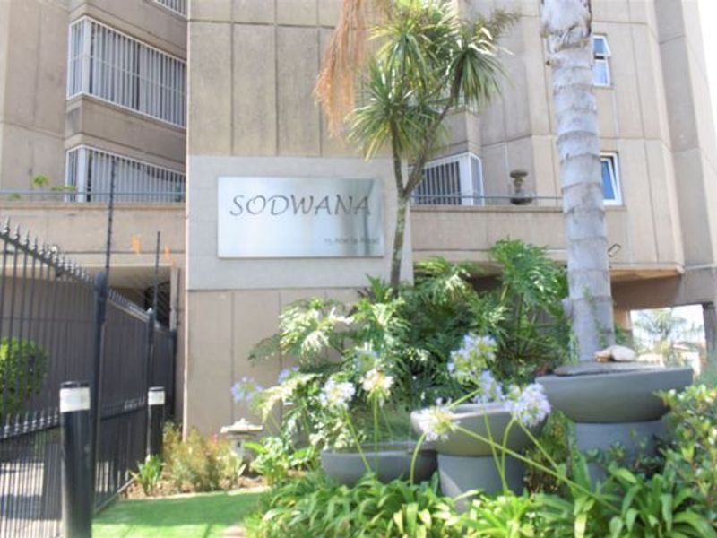 Front entrance view of the Sodwana apartment complex, featuring security fencing, established garden landscaping, and building signage.