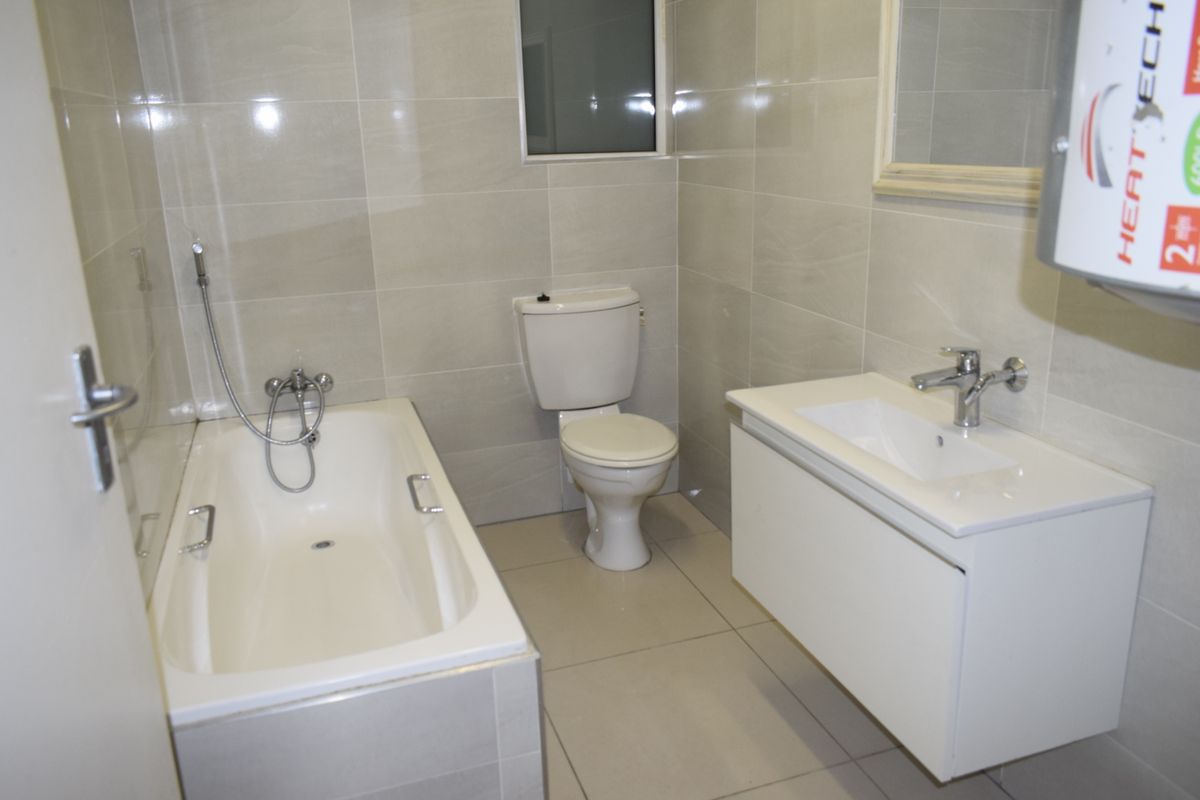 A clean, modern bathroom featuring a bathtub with handheld shower, a wall-mounted vanity with basin, and neutral floor-to-ceiling wall tiles.