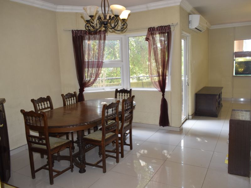 A dining area featuring tiled flooring, crown molding, and a split-system air conditioner, with natural light provided by large windows and a glass door.