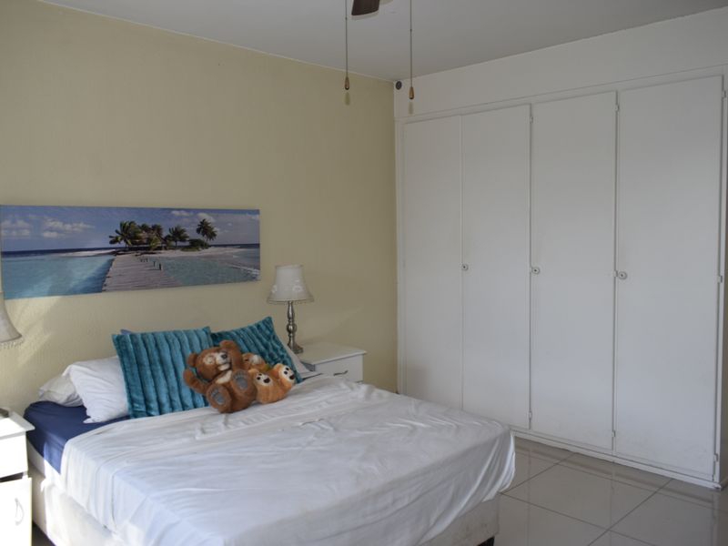 A bedroom featuring tiled flooring, a ceiling fan, and a large white built-in wardrobe providing ample storage space.