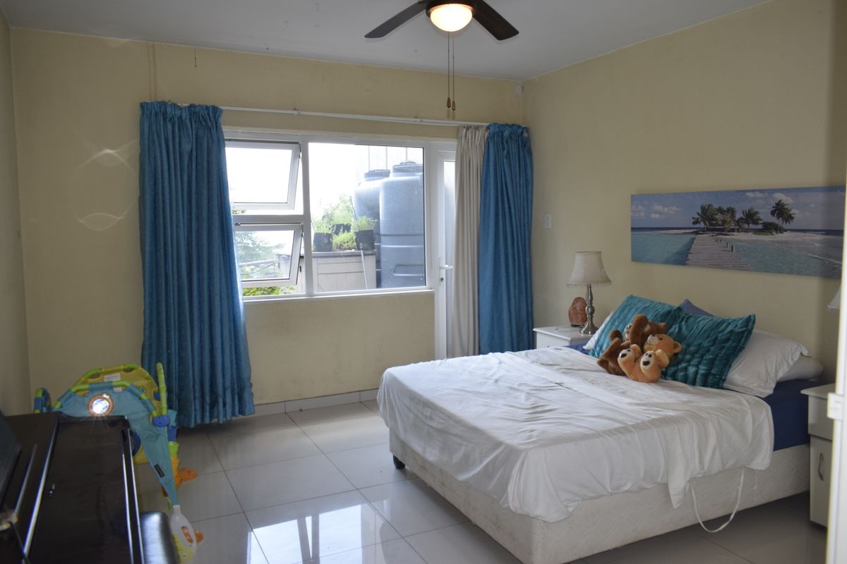 A spacious bedroom featuring tiled flooring, a ceiling fan, and large windows providing natural light and access to an outdoor area.