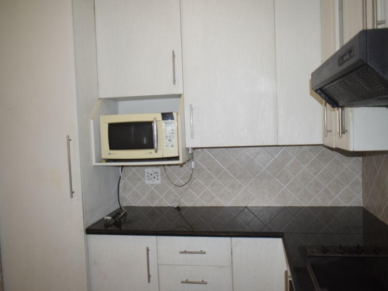 A functional kitchen featuring white cabinetry, dark granite countertops, a built-in hob, and an extractor fan with a tiled backsplash.