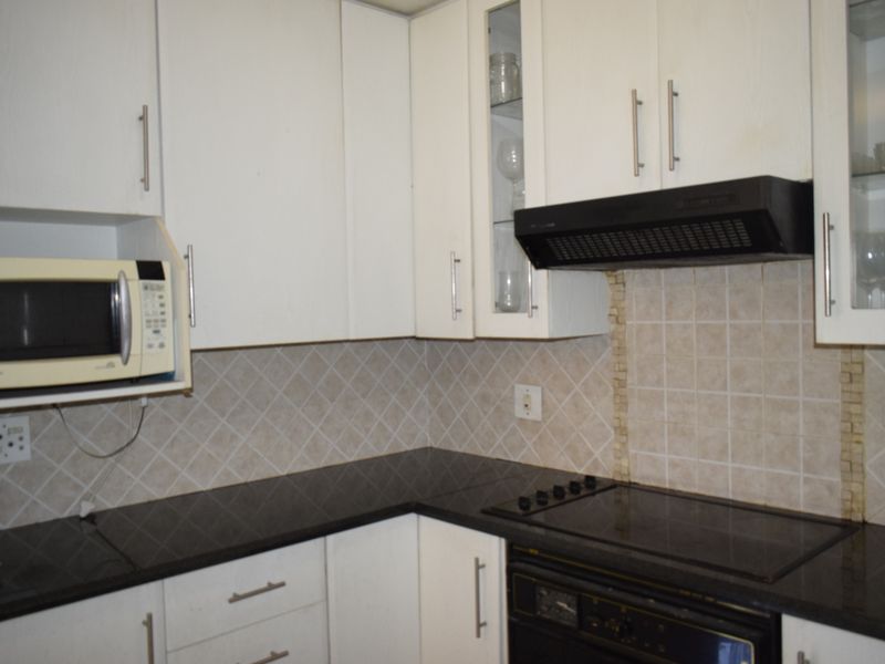 A functional kitchen featuring white cabinetry, dark granite countertops, a tiled backsplash, and integrated appliances including an oven, hob, and extractor fan.