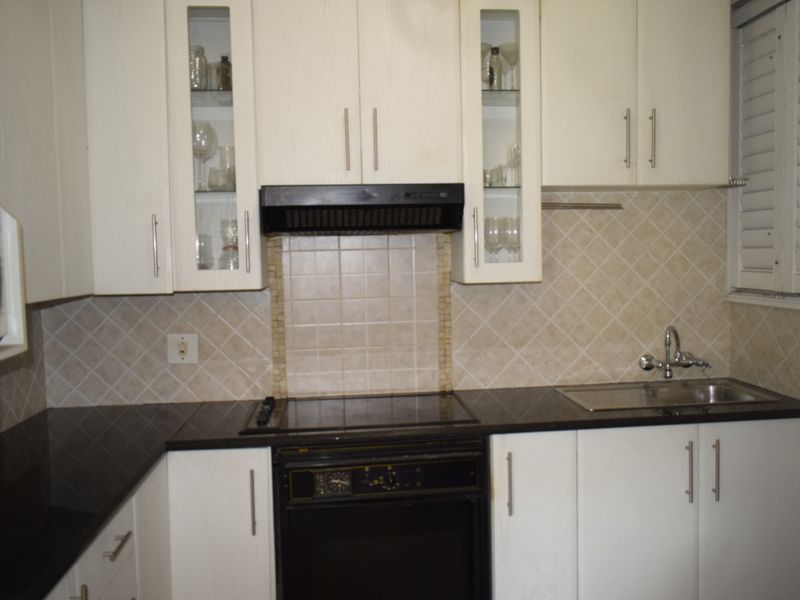A functional kitchen featuring white cabinetry, dark stone countertops, a built-in oven with hob, and a tiled backsplash.