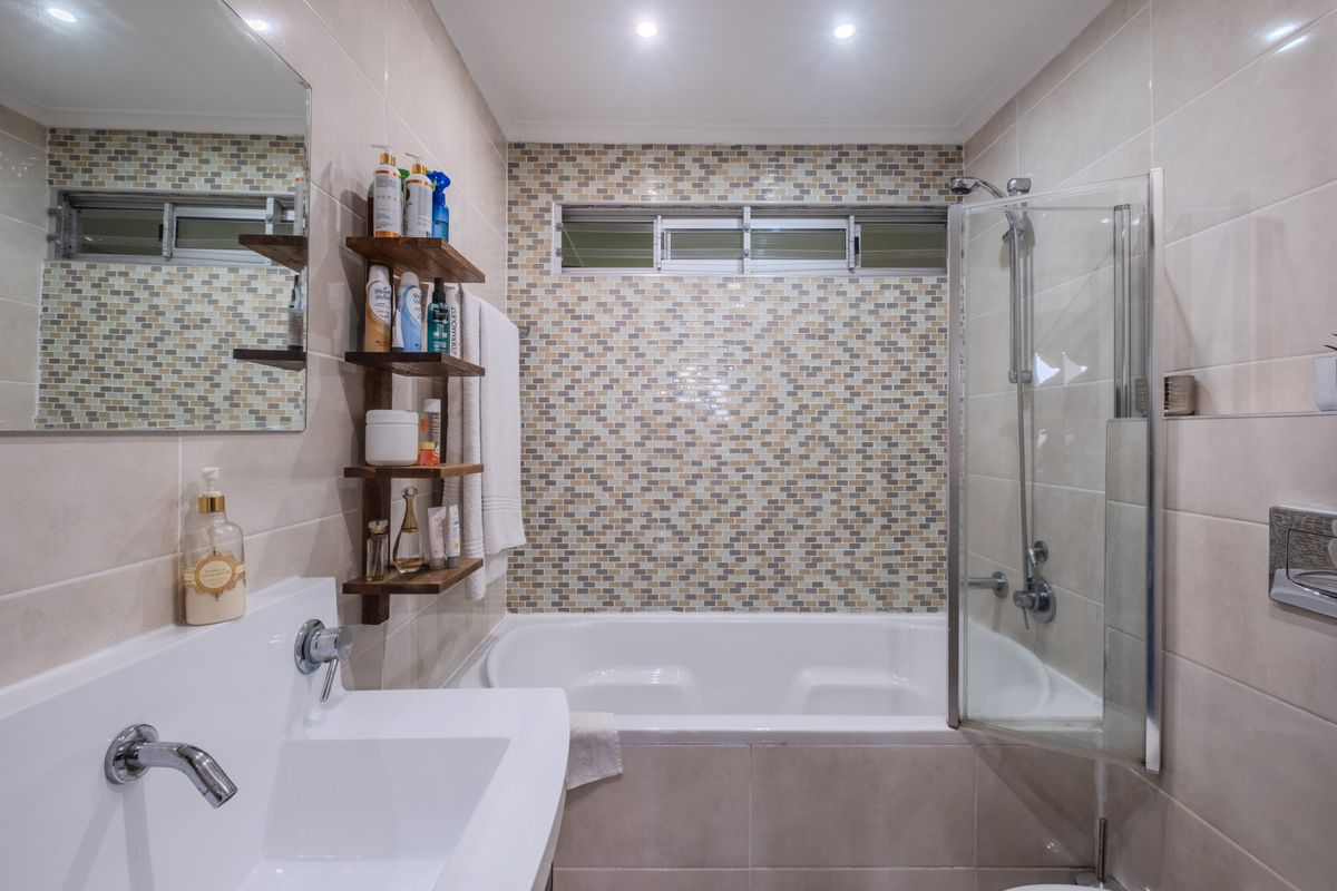 Modern bathroom featuring a built-in bathtub with a glass shower screen, a wall-mounted basin, and a decorative mosaic tile feature wall.