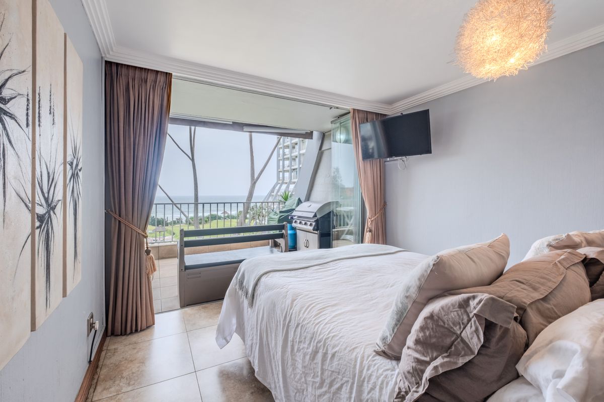 A well-maintained bedroom featuring tiled flooring, crown molding, and direct access to a private balcony with ocean views.