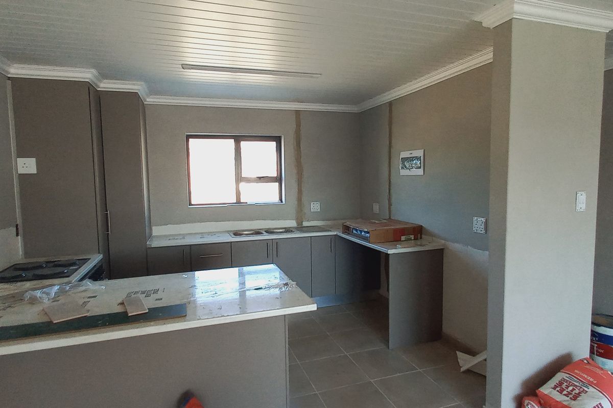 An unfinished kitchen space featuring built-in cabinetry, stone countertops, and a hob, currently undergoing renovation with exposed wall surfaces.