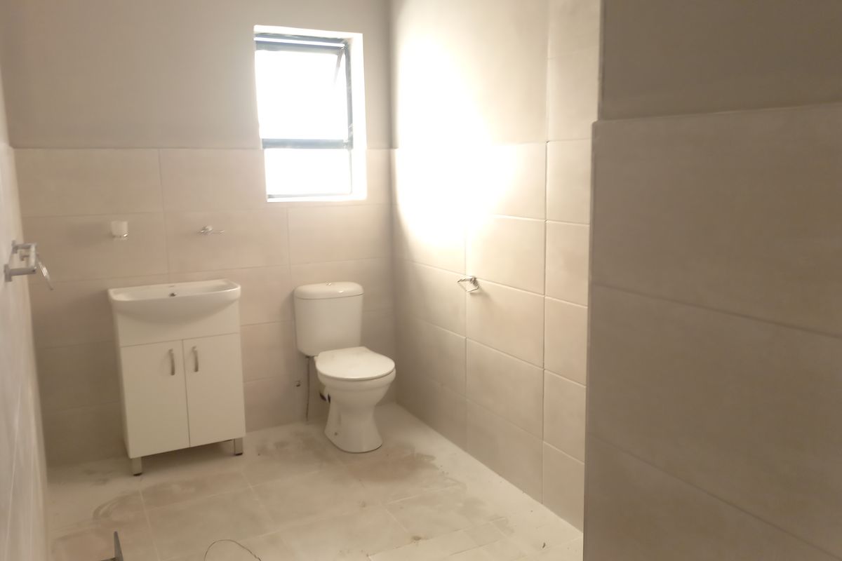 A clean, modern bathroom featuring neutral wall and floor tiles, a white vanity cabinet with basin, and a standard toilet.