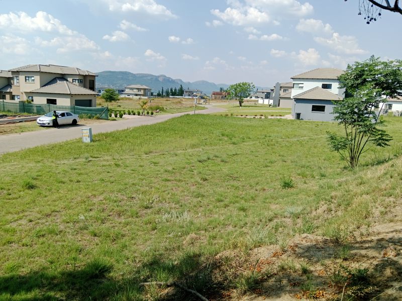A vacant residential plot featuring established grass cover, road access, and surrounding residential development with mountain views in a secure estate setting.