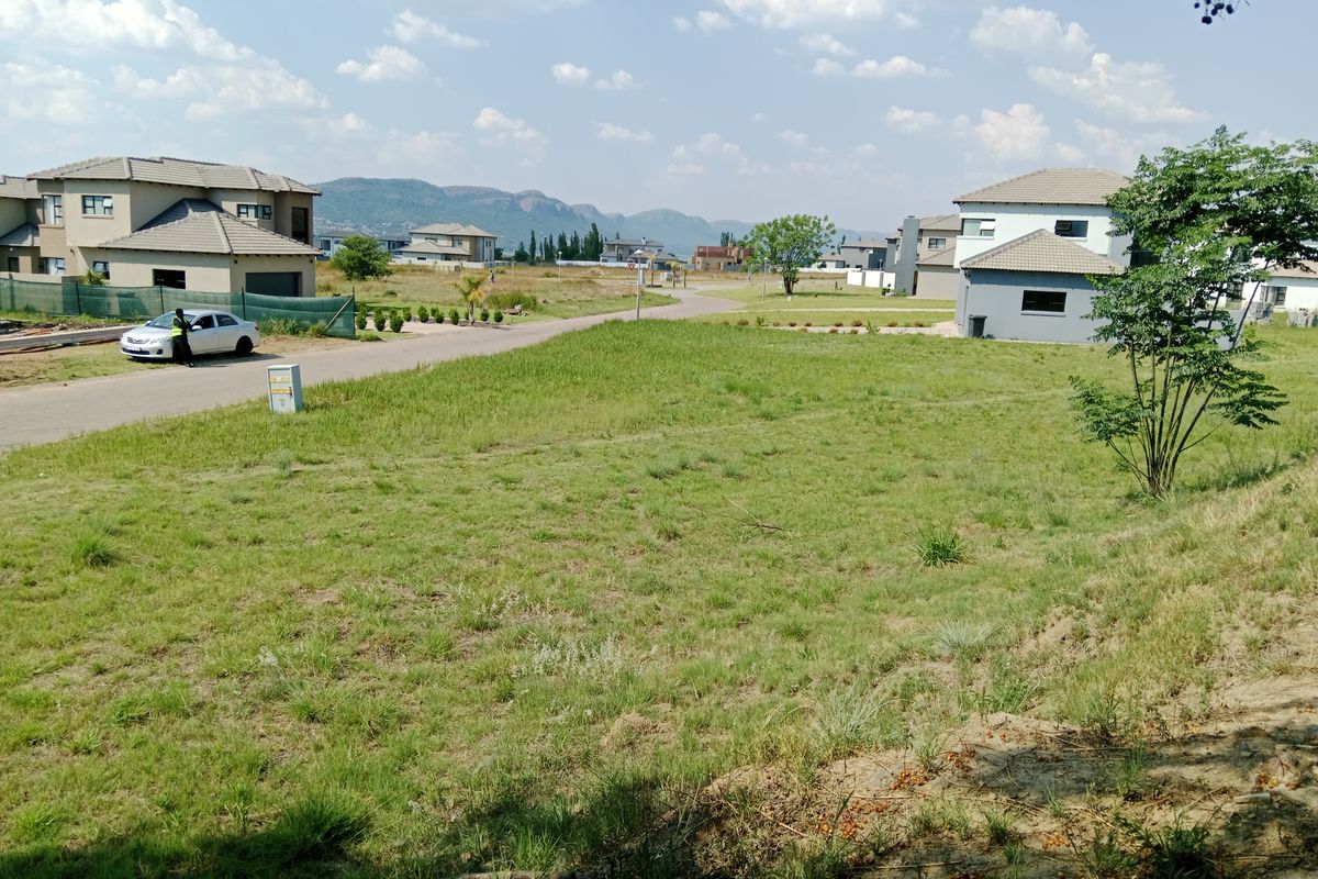 A vacant residential plot featuring established grass cover, road access, and surrounding residential development with mountain views in a secure estate setting.