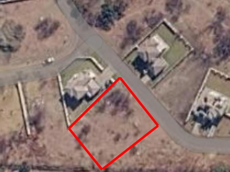 An aerial view of a vacant residential plot located in a suburban neighborhood, highlighted with a red boundary outline.