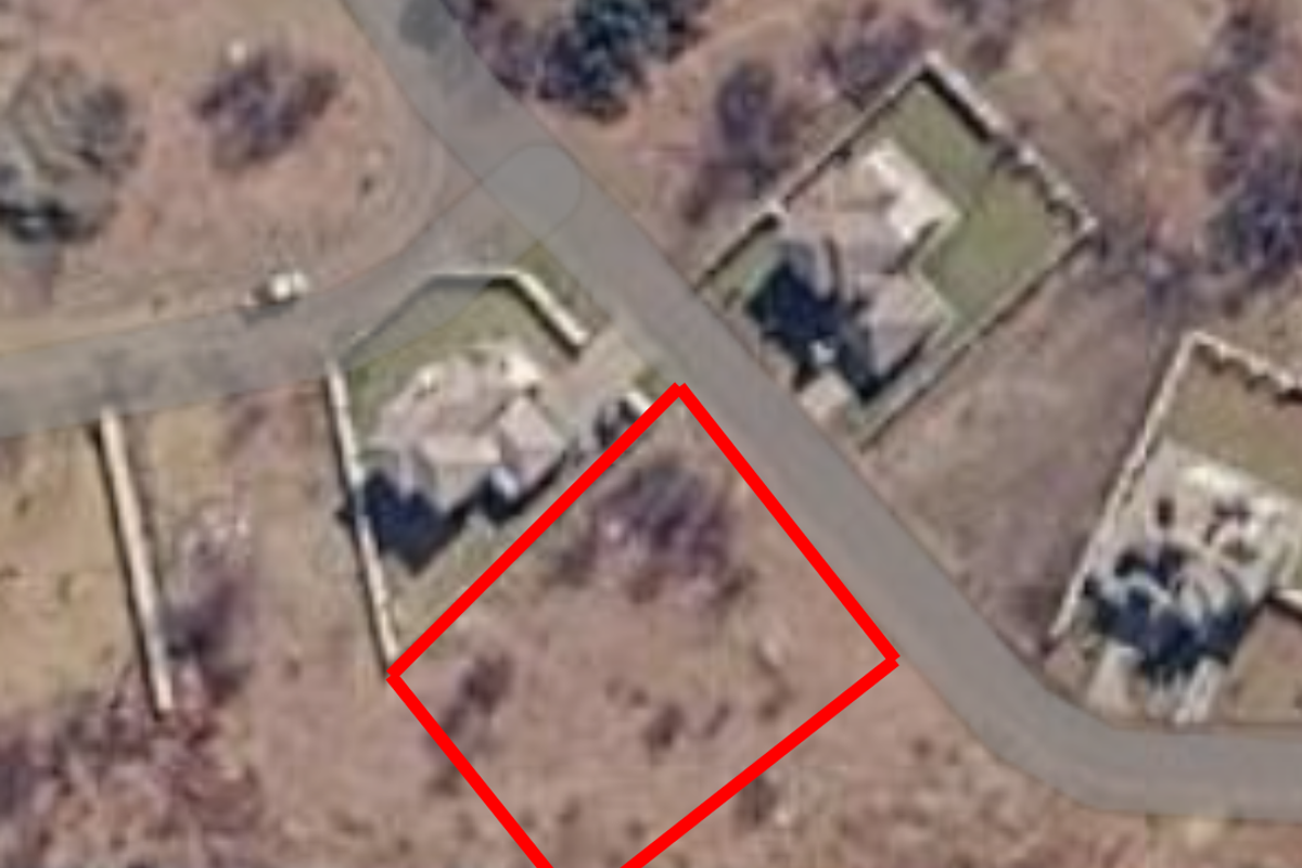 An aerial view of a vacant residential plot located in a suburban neighborhood, highlighted with a red boundary outline.