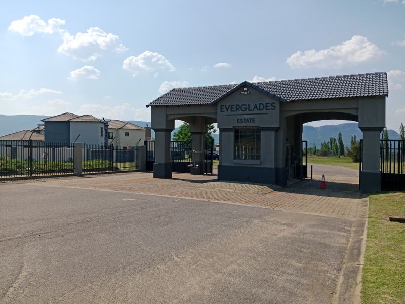 The main entrance gatehouse of Everglades Estate, featuring a paved driveway, secure perimeter fencing, and a well-maintained structure.