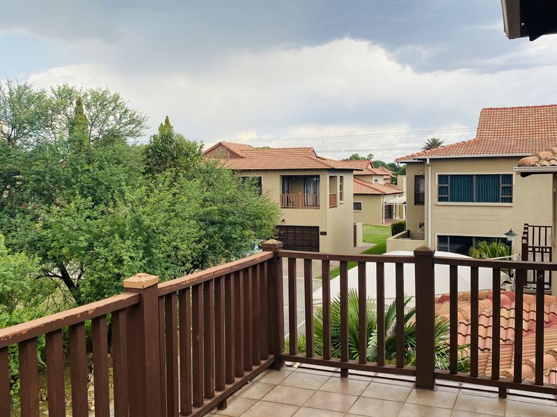 An elevated balcony featuring tiled flooring and a wooden balustrade, offering views of the surrounding residential estate.