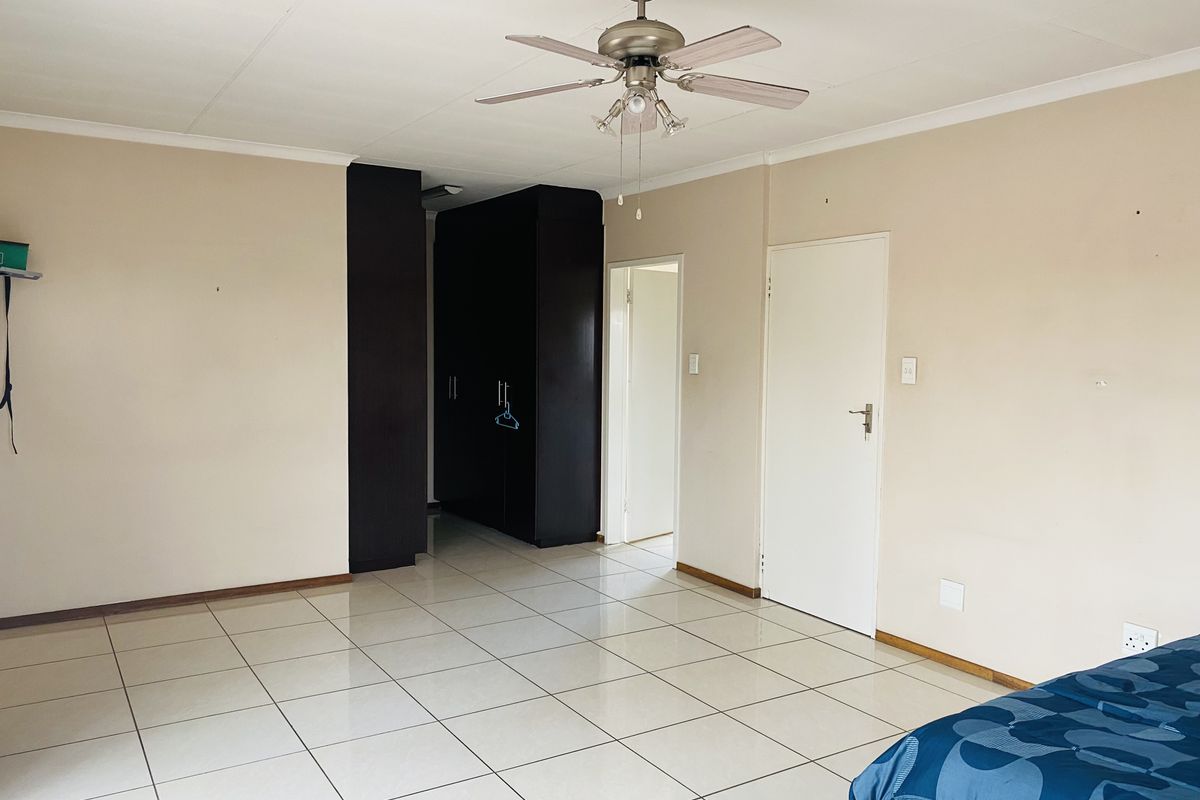 A spacious bedroom featuring neutral walls, tiled flooring, a ceiling fan, and built-in dark wood cupboards.
