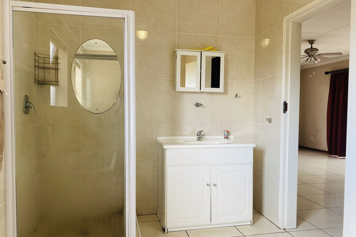 A functional bathroom featuring a shower enclosure, vanity cabinet with basin, and neutral wall tiling, offering a clean and practical space.