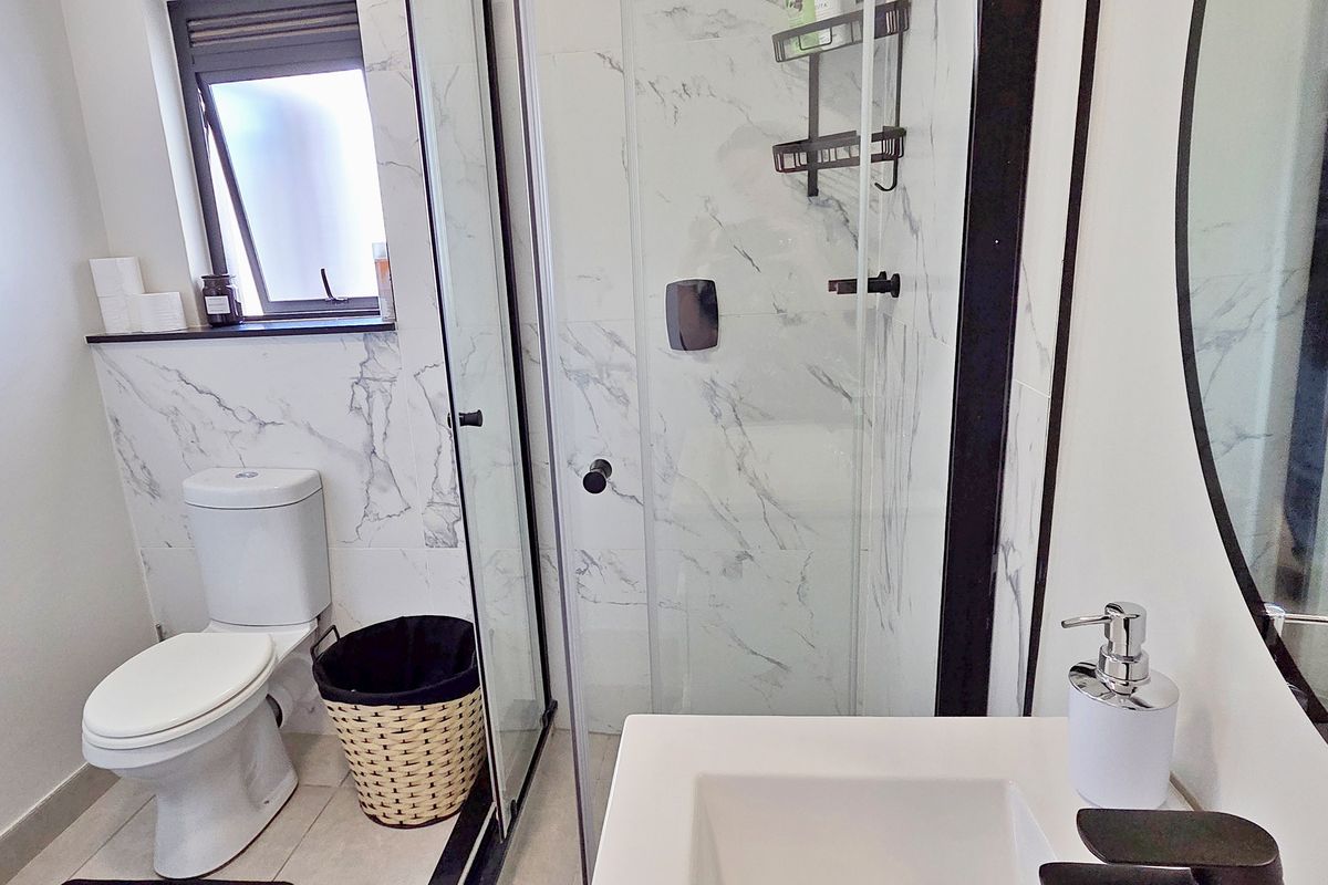 Modern bathroom featuring a walk-in shower with marble-look tiling, black fixtures, and a sleek vanity basin.