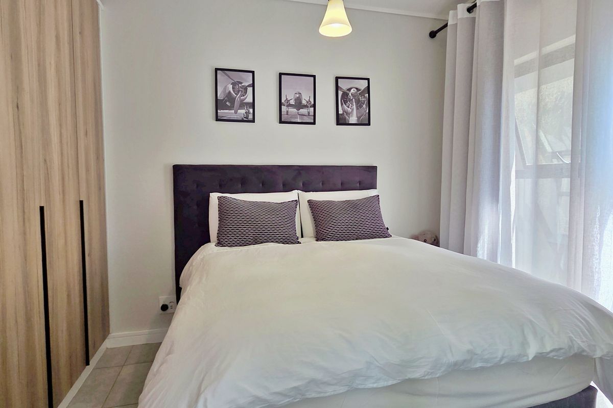A well-maintained bedroom featuring modern wood-finish built-in wardrobes, neutral tiled flooring, and natural light through large windows.
