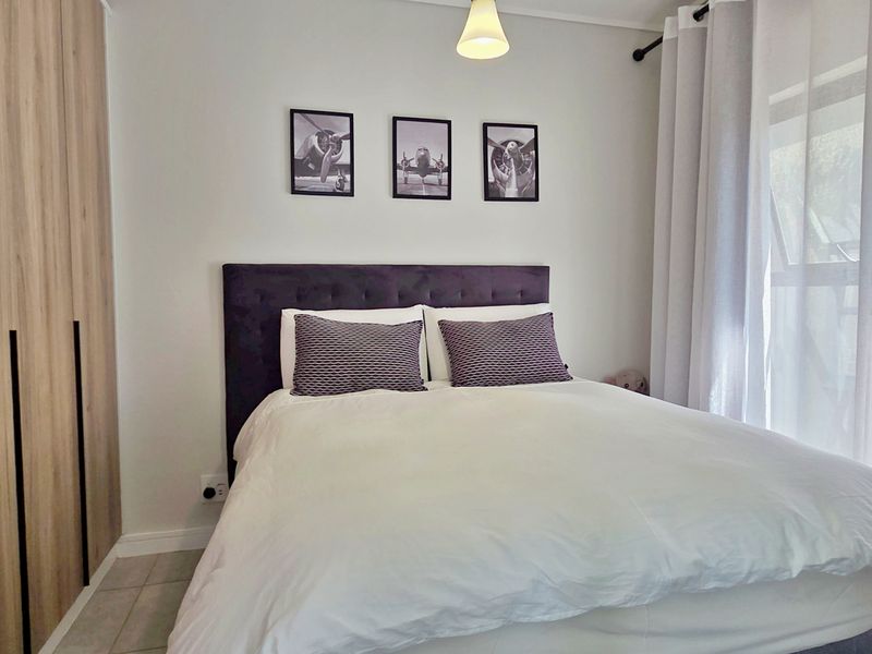 A well-maintained bedroom featuring modern wood-finish built-in wardrobes, neutral tiled flooring, and natural light through large windows.