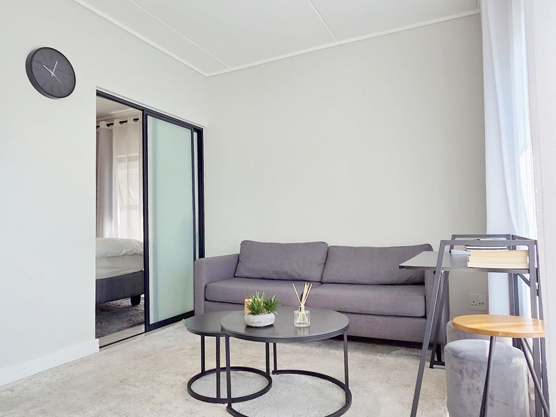 A bright open-plan living area featuring neutral finishes, modern cabinetry, and a sliding door providing access to the adjacent bedroom.