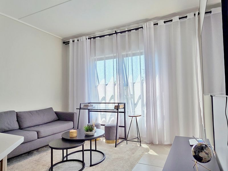 A bright and modern living room featuring tiled flooring and a large sliding glass door with sheer curtains, providing ample natural light.